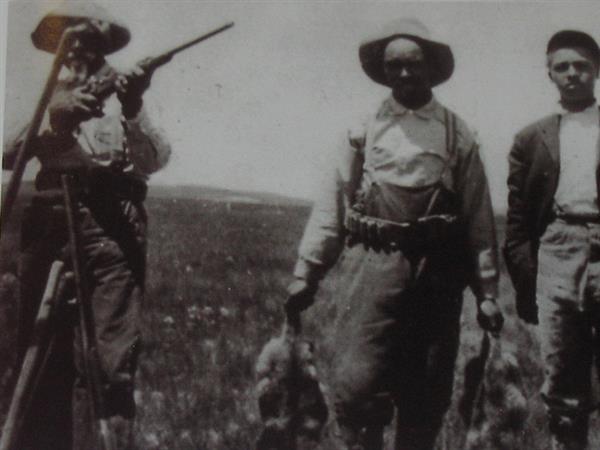 Three black men hunting, one holding a rifle and one holding results of the hunt
